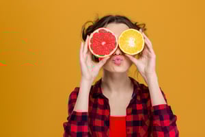 Woman being joyful holds oranges on eyes.  - The Trifecta of Joyful Leadership