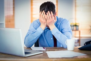 Stressed man with hands on head sitting at desk while working. - Five Struggles Every Business Owner Faces and How a Franchise Could Help