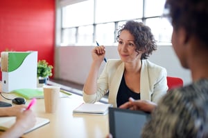 Woman writing at table with co-workers - 8 Steps To Being More Confident At Work