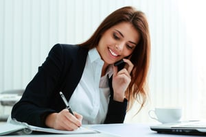 Woman on cell phone while writing. - Questions to Ask a Franchisor During a Validation Call
