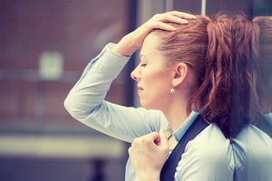 Woman places hand on forehead. - Corporate Burnout? Consider Owning a Franchise