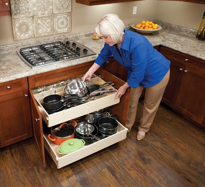 A white-haired woman smiles as she pulls out her kitchen cabinet shelving and reaches for a pot.